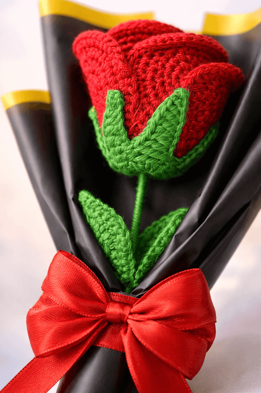 Knitted red rose with green leaves and a red bow on a black background
