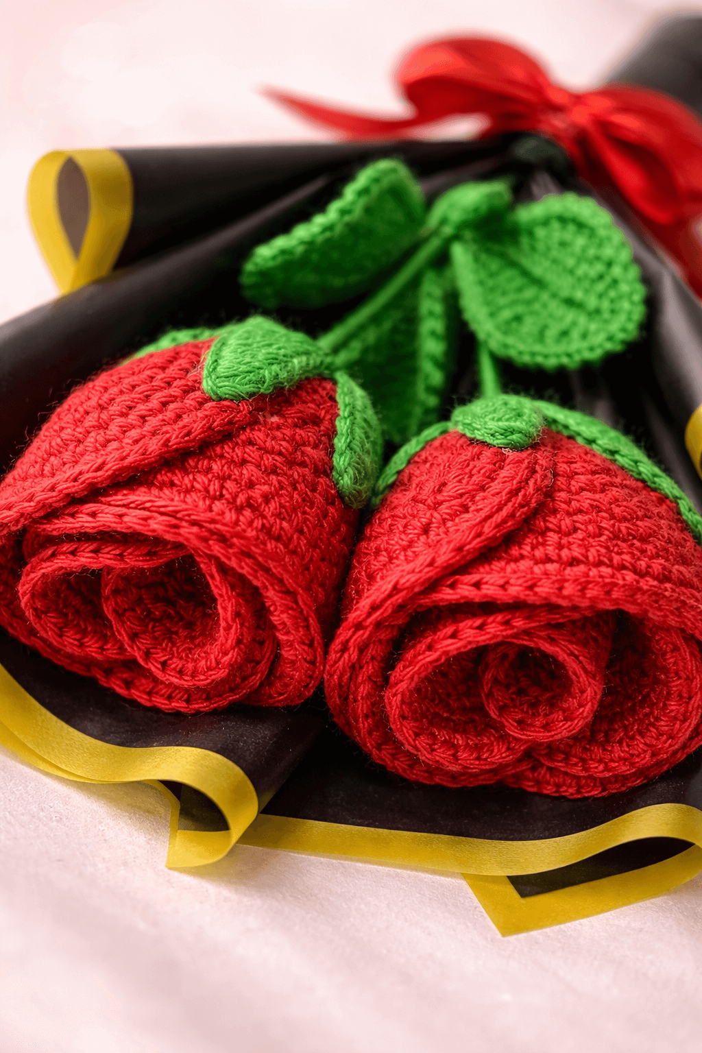 Knitted red roses with green leaves on a black background
