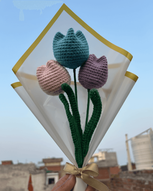 Knitted tulips in blue, pink, and purple held against a clear sky.
